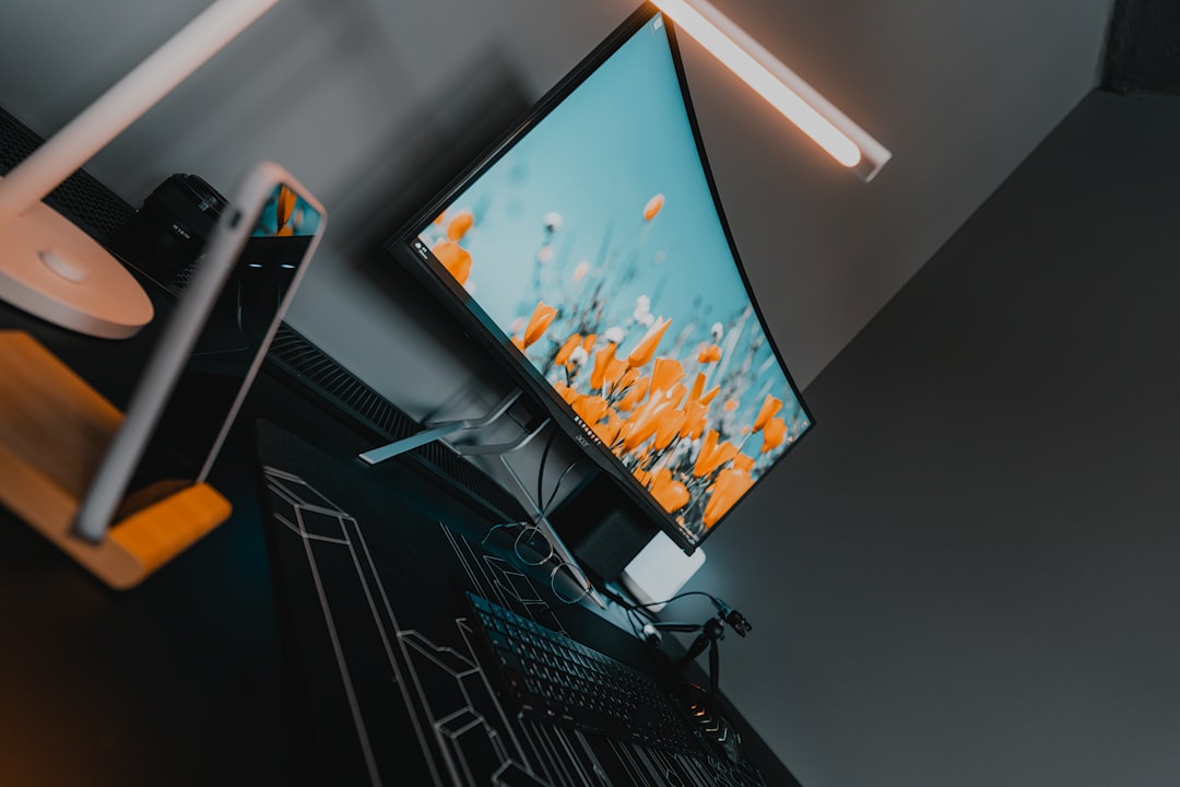 A computer monitor displaying orange flowers on a desk with a keyboard and lamp